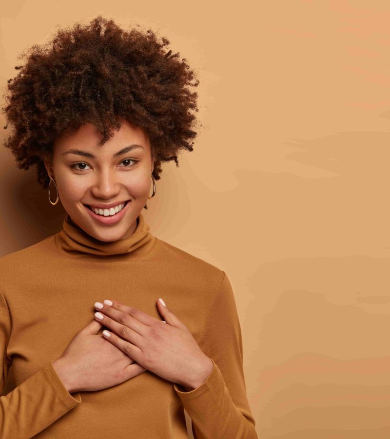 pleased-charming-woman-with-afro-hairstyle-receives-nice-gift-presses-hands-heart-appreciates-help-smiles-gently-feels-very-grateful-min